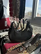 Cartera negra con forma de media luna, asa corta y detalle de estrella plateada.