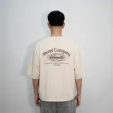 Remera color beige de corte oversize con estampado en la espalda que dice "Secret Company Venelo" y una cita bíblica.