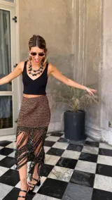 Falda corta tejida a mano en crochet, con diseño a rayas horizontales en tonos marrón oscuro y dorado brillante. Presenta un borde inferior con flecos largos y abundantes.