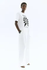 Remera de manga corta y cuello redondo, color blanco, con estampado frontal en negro que incluye la palabra "FLEURI", una ilustración abstracta de una hoja o flor y el texto "LA BEAUTÉ DE LA NATURE PARIS, 1978".