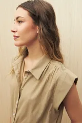 Camisa color beige, de corte recto, con cuello clásico, mangas cortas con volados en los hombros y cierre frontal con botones.