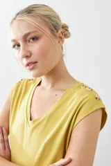 Remera verde pistacho de corte recto, con cuello en V y botones decorativos en los hombros.