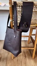 Bolso tote de cuero color marrón oscuro con doble asa larga de cuero y remaches metálicos.