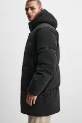 Cazadora acolchada negra de tejido técnico, cuello alto con capucha ajustable, manga larga con puño interior elástico, bolsillos laterales y bolsillo interior. Cierre frontal con cremallera oculta y botones a presión.