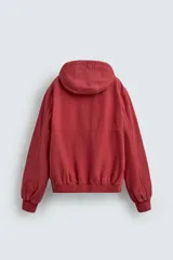 Cazadora relaxed fit color ladrillo confeccionada en tejido de algodón con estructura canvas. Tiene cuello con capucha ajustable, manga larga, bolsillos frontales de vivo, acabados con rib elástico, efecto lavado y cierre frontal de cremallera.
