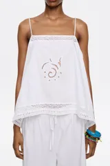 Top blanco de breteles finos, escote recto y corte holgado. Presenta bordados calados y terminaciones de encaje.