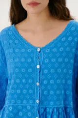 Camisa blanca con bordado floral, cuello en V y cierre frontal con botones.