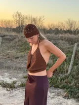 Top de crochet en hilo marrón con acabado brilloso. Diseñado con espalda libre y tiras ajustables que se atan atrás, este top realza la figura y suma un toque bohemio y sofisticado a cualquier look.