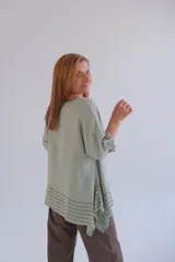 Blusa verde claro de lino, corte holgado, con cuello redondo y mangas 3/4. Presenta un diseño asimétrico con terminación en puntas y detalle de líneas horizontales negras en el ruedo.