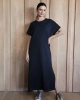 Vestido largo color crudo con cuello redondo y mangas cortas con ribete negro. Tiene corte recto y aberturas laterales en el ruedo.