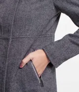 Saco largo de polivelour con textura espina de pez en tonos grises. Tiene cuello alto, capucha, cierre delantero con botón y cremallera, manga larga y bolsillos.