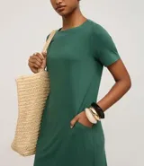 Vestido corto de mujer, estilo camiseta, color terracota/óxido, con escote redondo, mangas cortas y bolsillos laterales. El bajo es redondeado.