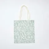Tote bag de tela color celeste con estampado de hojas blancas.