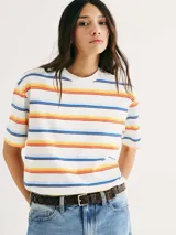 Camiseta de manga corta con cuello redondo, color blanco, con un patrón de rayas horizontales en tonos cálidos y azules (naranja, amarillo, rojo, azul oscuro y celeste).