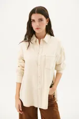 Camisa beige de corte recto, con cuello clásico, cierre frontal con botones, bolsillo en el pecho y mangas largas con puños abotonados.