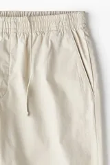 Pantalón color beige de popelina de algodón, corte ancho, con cintura elástica ajustable con cordón, bolsillos laterales y traseros.