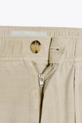 Pantalón gris oscuro de tiro alto con cintura elástica, bolsillos delanteros y falsos bolsillos con solapa en la espalda. Cierre frontal con cremallera y botón.