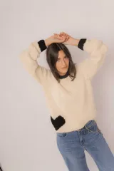 Sweater tejido de lana merino color crema, con cuello redondo y puños negros. Tiene un corazón negro en el frente.