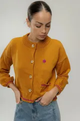 Cardigan color mostaza de tejido de punto con botones, cuello redondo, mangas largas y detalle de bordado floral en el pecho.