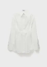 Camisa blanca de algodón con diseño entallado, cuello camisero, mangas largas con detalle metálico y cierre frontal de botones oculto.