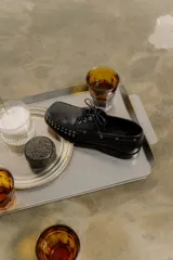 Mocasín de cuero color marrón con tachas metálicas plateadas en la puntera y laterales.