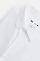 Camisa blanca de algodón, corte slim fit, cuello italiano, manga larga con puños abotonados y cierre frontal con botones.