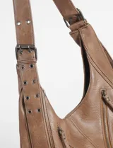 Cartera hobo color crudo de cuero sintético, con correa de hombro ajustable y múltiples cierres decorativos en el frente.
