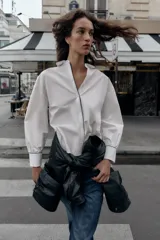 Camisa blanca de popelín con vivos negros a contraste en el cuello, el frente y los puños. Presenta un corte holgado y mangas largas con puños anchos.