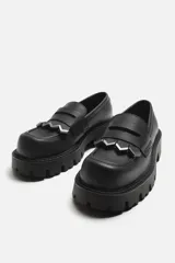 Mocasín negro de cuero con antifaz y flecos con puntas metálicas en el empeine, horma cuadrada y suela con volumen.