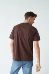 Remera marrón de algodón con cuello redondo, corte regular y estampado en el pecho. El modelo usa talle M.