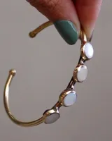 Pulsera rígida dorada con cuatro piedras circulares de nácar engarzadas.