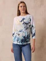Buzo blanco estampado con flores azules y detalles en verde y amarillo, de la marca Milano. Tiene cuello redondo y mangas 3/4 con apliques de brillos en el frente.