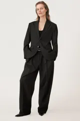Pantalón negro de tiro medio con cintura con trabillas, bolsillos laterales y con solapa en espalda. Detalle de pinzas y raya planchada en delantero. Cierre frontal con cremallera, botón y ganchos metálicos.