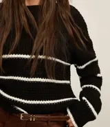 Suéter de punto pesado color negro con rayas horizontales blancas, cuello redondo y mangas largas con sisas desplazadas.