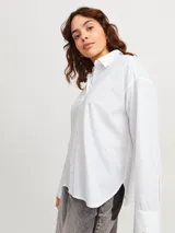 Camisa blanca de corte oversize con cuello clásico, cierre frontal con botones y pequeños brillantes plateados distribuidos por toda la prenda.
