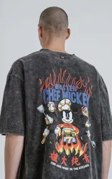 Remera de algodón premium color gris oscuro con efecto nevado (acid wash), corte oversize y manga corta. Estampa trasera con el personaje de Mickey Mouse vestido de chef rodeado de llamas y utensilios de cocina, con texto en inglés y chino.