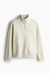Buzo color crema de tejido pesado con interior cepillado, cuello elevado, medio cierre y hombros caídos. Puños y bajo en punto acanalado. Corte estándar.