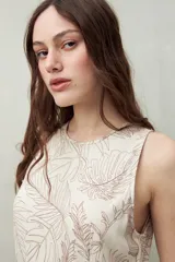 Vestido largo sin mangas con diseño cruzado y lazo lateral. Confeccionado en mezcla de lino y viscosa, presenta un estampado sutil de hojas en tonos marrones sobre un fondo beige y una abertura frontal que aporta movimiento.