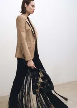 Blazer color beige de gamuza, con cuello de solapa, cierre de un botón, dos bolsillos frontales con solapa, mangas largas con puños abotonados y forro interior.