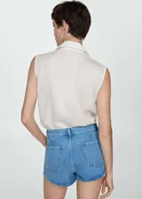 Camisa blanca sin mangas con cuello clásico, cierre frontal con botones y bolsillo de parche en el pecho.