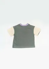 Remera marrón con mangas cortas color mostaza, cuello redondo color crema y estampado frontal con la frase "Vigilante Peacemaker Quotes".