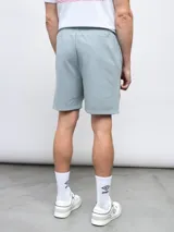 Bermuda gris de felpa sin friza, con cintura elástica ajustable con cordón y logo Umbro estampado en rojo en la pierna izquierda.