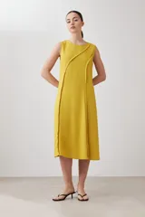 Vestido midi acampanado color mostaza, sin mangas, confeccionado en lino con detalle desflecado en los bordes. Incluye una bufanda del mismo material y color.