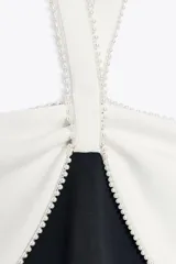 Vestido midi negro de tejido elástico, con escote recto y cuello halter. Presenta un lazo blanco a contraste en el delantero con aplicación de perlas y espalda descubierta.