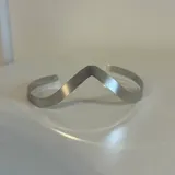 Brazalete metálico con diseño ondulado y acabado mate.