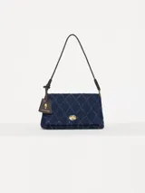 Bandolera confeccionada en denim azul con diseño acolchado en forma de rombos. Tiene correa de cuero marrón, cierre con torniquete metálico dorado y tag colgante con aplique de hongo.