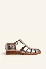 Sandalia plateada de cuero vacuno con diseño de tiras entrecruzadas, puntera redondeada y hebilla lateral. Tiene un taco bajo de 2,5 cm y suela de cuero.