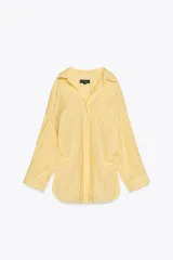 Camisa oversize a rayas amarillas y blancas, de cuello solapa y manga larga tipo murciélago acabada en puño con hombro caído. Tiene un bolsillo de plastrón en el delantero y cierre frontal con botones.