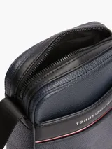 Bandolera Tommy Hilfiger de poliuretano granulado color azul marino, con correa ajustable de tejido jacquard con el logo de la marca. Tiene un compartimento principal con cierre, bolsillo interior con cremallera y bolsillo exterior abierto.