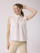 Blusa blanca de algodón con bordado en el canesú, cuello alto con volantes y mangas cortas con volantes.
